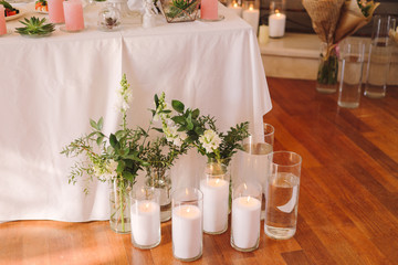Coziness and style. Modern event design. Table setting at wedding reception. Floral compositions with beautiful flowers and greenery, candles, laying and plates on decorated table.