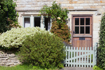 Dark brown doors in an old traditional English lime stone house with shrubs in a small front garden enclosed by dry stone fence, wooden gate .
