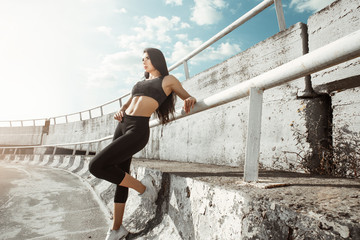 Fototapeta na wymiar Portrait of beautiful brunette. Sexy girl rest after running. Female fitness model working out outdoor in city. Young woman jogger athlete training on road. Concept of healthy lifestyle.