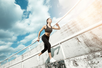 Fototapeta na wymiar Beautiful brunette in a start position. Young woman jogger athlete training on road. Concept of healthy lifestyle. Female fitness model working out outdoor in city.
