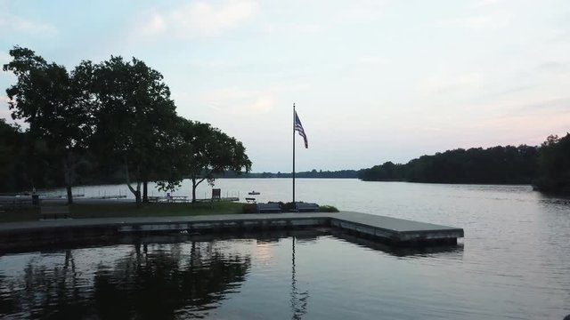 Aerial, American flag waves over lake in Milford, Michigan
