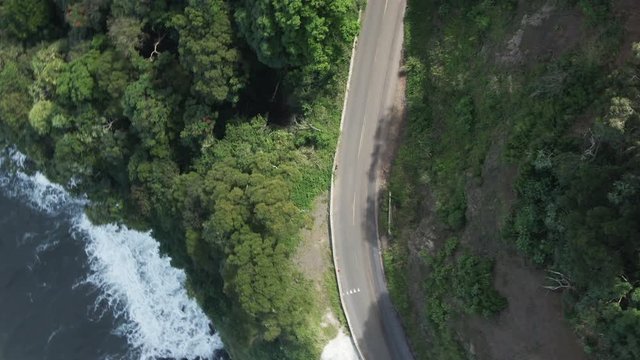 Overhead aerial, car drives along cliff on Road to Hana in Hawaii