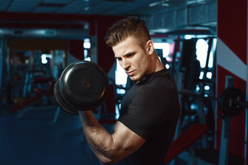 Fototapeta na wymiar Muscular model sports young man exercising in gym with dumbbell. Portrait of sporty healthy strong muscle. Fitness trainer. Sport workout bodybuilding motivation concept.