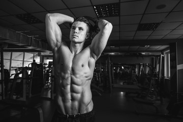 Muscular model sports young man exercising in gym with dumbbell. Black and white portrait of strong muscle. Fitness trainer. Sport workout bodybuilding motivation concept. Sexy torso.