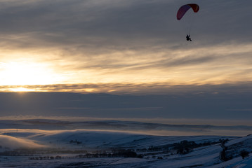 A Paraglider taking flight in the middle of winter against the sunset