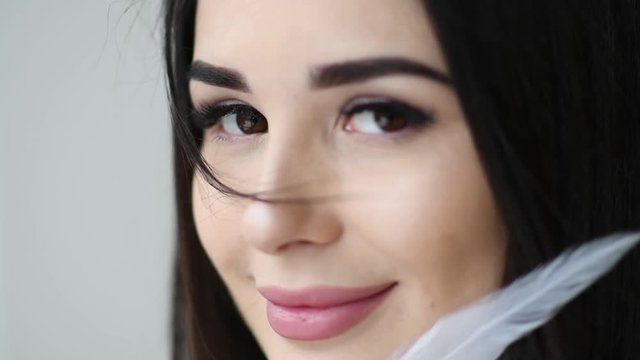 Close up portrait of beautiful woman play with feather sexy near her face with makeup and long eyelashes