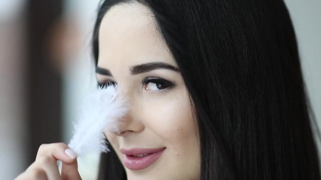 Close up portrait of beautiful woman play with feather sexy near her face with makeup and long eyelashes