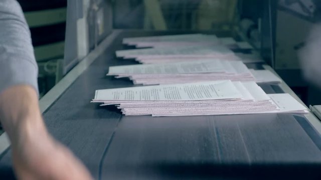 People take paper from typographical conveyor, close up.