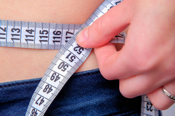 Close up woman measuring her waistline as symbol of diet and healthy lifestyle.