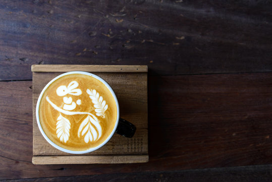 Top view a cup of hot coffee cappuccino with cute signature rabbit, flower and leaf latte art pattern in black ceramic cup on rough wooden tray and table. 