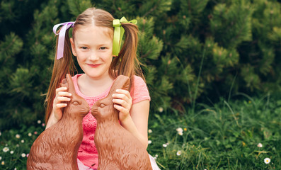 Outdoor portrait of a cute little girl playing in a garden with two chocolate bunnies