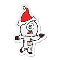 sticker cartoon of a cyclops alien spaceman pointing wearing santa hat
