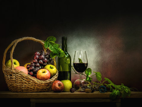 wine bottle with glasses and basket of red grapes and apple on wooden table and background