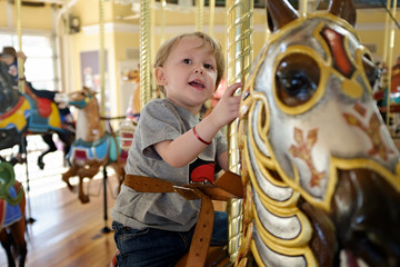 Young blond ,toddler aged ,blond haired boy ,riding a brown carousel horse on a merry go round