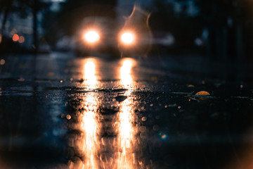 Night road blurred. Headlight of car in the dark while heavy raining. Rain in the city. Road, pavement, close up. Water splashes, spills on roadway