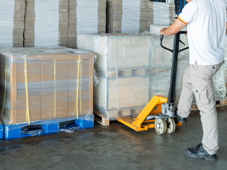 Man worker with hand pallet truck moving a goods pallet in warehouse.