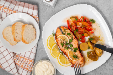 Baked salmon fillet medallion with salad of pickled vegetables and mushrooms on a white plate on a gray background, top view, flatlay