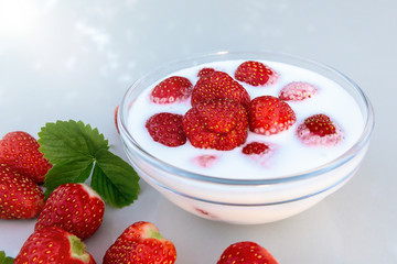 Fresh ripe strawberries in a bowl with yogurt on a white table outdoors on a summer day