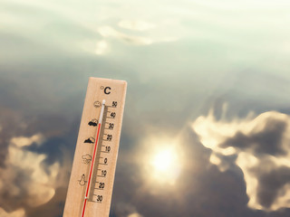 Thermometer showing 30 degrees of heat against the backdrop of lake water with the reflection of clouds and the sun