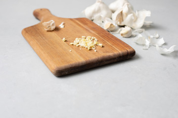 Minced Garlic on Wooden Cutting Board with Garlic Cloves and Bulbs in Background on Gray Countertop