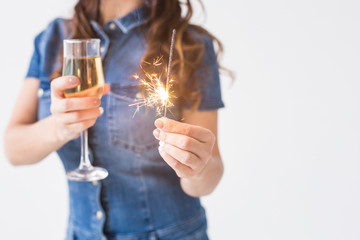 Celebration, drinks and holiday concept - close up of young woman with sparkler and glass of champagne on white background