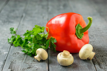 Ripe red pepper with parsley leaves and mushrooms on a black wooden table. Vegetarian food.