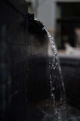 Close Up of Water Flowing Over the Edge of a Dark Stone Water Fountain