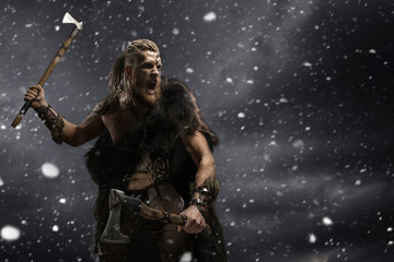 Fototapeta na wymiar Medieval warrior berserk Viking with tattoo and in skin with axes attacks enemy. Concept photo
