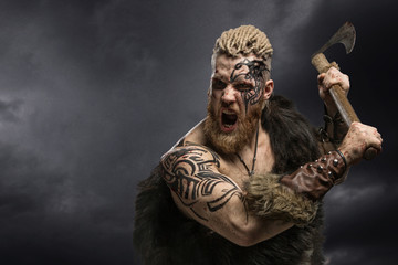 Medieval warrior berserk Viking with tattoo and in skin with axe attacks enemy. Close-up portrait