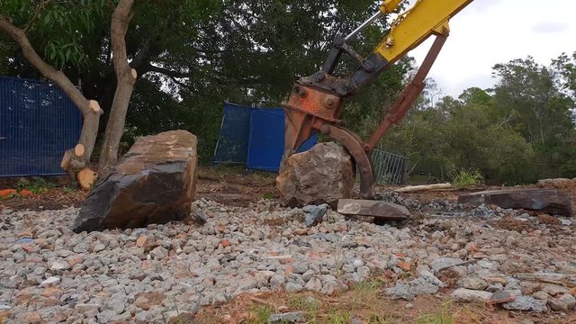 A large excavator lifting a heavy boulder on a construction site