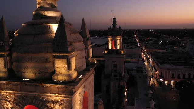Aerial camera at night very close to and one of the bell towers of the Cathedral of Merida, Yucatan, Mexico and descending.