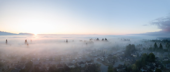 Aerial view of a residential neighborhood covered in a layer of fog during a vibrant sunrise. Taken in Greater Vancouver, BC, Canada.