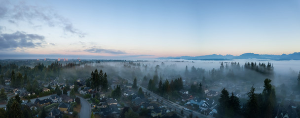 Aerial view of a residential neighborhood covered in a layer of fog during a vibrant sunrise. Taken in Greater Vancouver, BC, Canada.