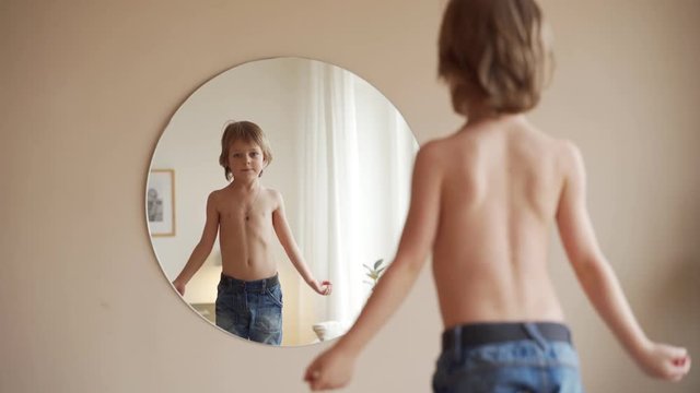 Confident kid looking at his muscles in mirror imagining that he is super hero