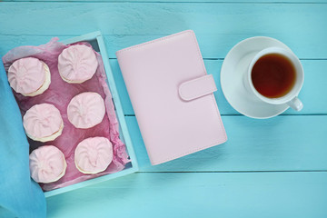 Spring tea.Flat lay..pink marshmallow and pink diary, cup of tea and white flowers on a blue wooden board background.top view, copy space.Spring mood