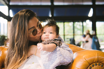 Happy family mother lifting and kissing with newborn baby in a nice cafe.