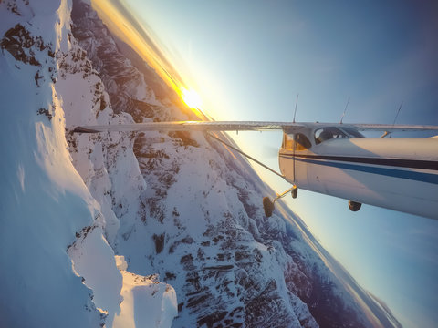 Small airplane flying near the rocky Candian Mountains during a vibrant sunset. Taken North of Vancouver, British Columbia, Canada.