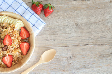 Healthy breakfast ingredients with granola, strawberry, banana and almond in wooden bowl and wooden spoon on table.