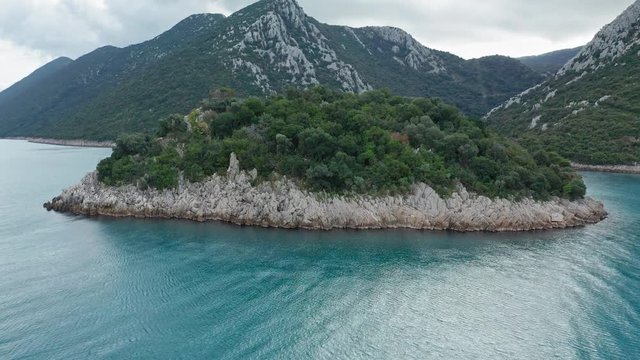 Detail of an island in Divna and some buildings on its beach on a cloudy day. Cres Island. Croatia. Aerial view revealing