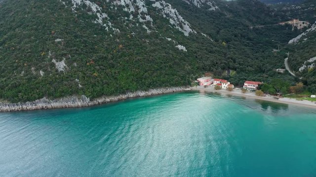 Beautiful landscape of the beach of Divna with some buildings and its calm and colorful waters. Cres Island. Croatia. Aerial view traveling backwards