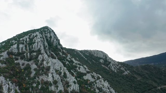Beautiful mountainscape revealing the beach of Divna with some buildings and its waters on a cloudy day. Cres Island. Croatia. Aerial view traveling backwards