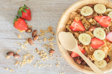 Healthy breakfast ingredients with granola, strawberry, banana and almond in wooden bowl and wooden spoon on table.