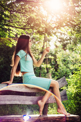 Wonderful spring. Beautiful young girl enjoys nature and sunlight sitting on a wooden bench in the park.