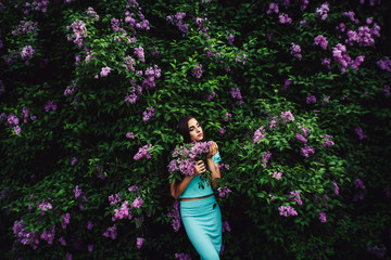 Wonderful spring. Cute young girl enjoys nature among the blossoming lilac and holds a bouquet.