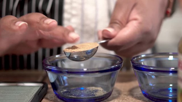 Woman shaking ground cumin into tablespoon and pouring into bowl, Close Up