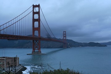 Golden gate bridge on dark, cloudy day with hills in background