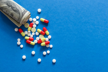 Various medicines and pills on background of USA dollars banknotes on dollar money isolated on blue background. 