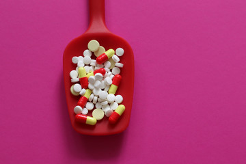 Medicine expenses. Various medicines and pills on red spoon isolated on pink background. 