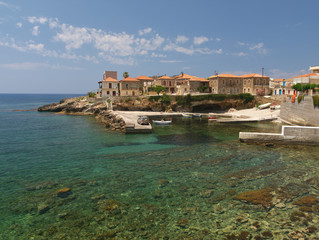 Fototapeta na wymiar Crystal clear water beach with rocks and stone village houses under day light in Mani, Greece.