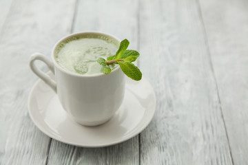 cup of hot matcha green tea with branch of mint on a grey background